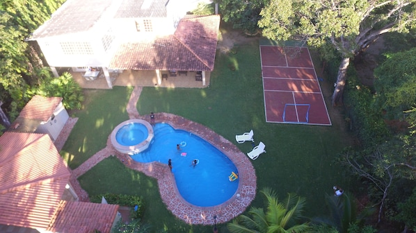 Un jardin avec une piscine, un court de tennis et une maison avec un toit en tuiles.