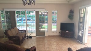 A spacious living room with wicker furniture, a television, and a sliding glass door leading to a patio. - Panama Santa Clara Beach Residence (Cocle)