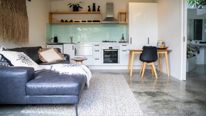 A modern kitchen with white cabinets, a black countertop, and a wooden dining table. -  BEACHWOOD STUDIO-a perfectly styled getaway for couples BEACH AT YOUR DOORSTEP (Smiths Beach)