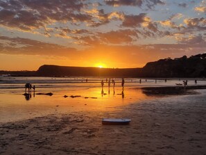 A beach scene with people walking, a sunset, and a cliff in the background. -  BEACHWOOD STUDIO YOUR BEACH ESCAPE STARTS AT YOUR DOORSTEP (Smiths Beach)