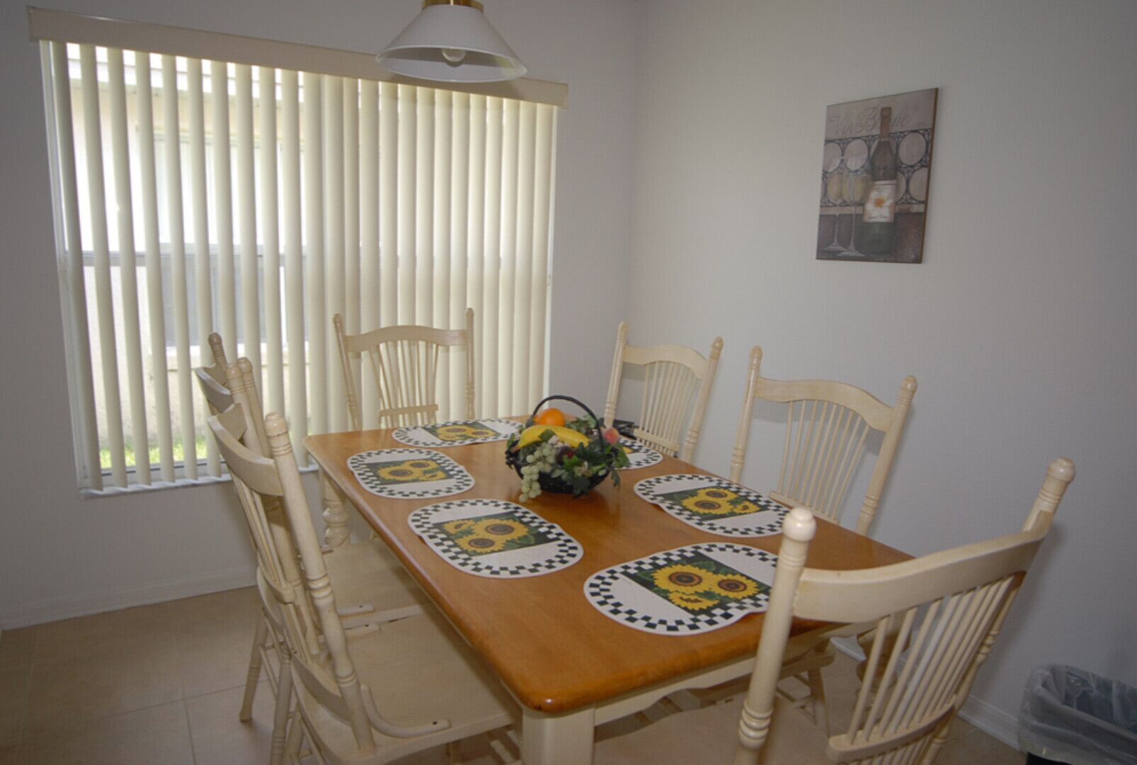 Uma sala de jantar com uma mesa de madeira posta para quatro pessoas, rodeada por cadeiras brancas.