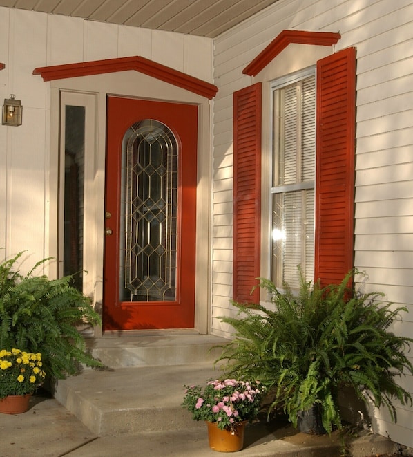 A house with a red door, a window with shutters, and potted plants on the porch.