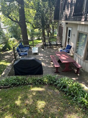 A covered patio with a table and chairs, surrounded by greenery and trees.
