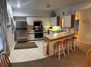 A modern kitchen with a refrigerator, stove, microwave, and bar stools.