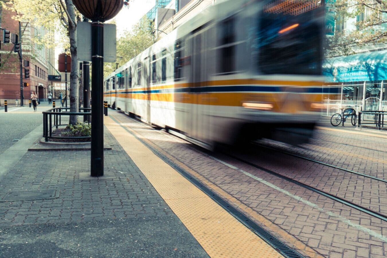 A train moving on a city street with a sidewalk and a tram stop.