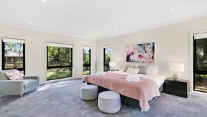 A modern bedroom with a large bed, two bedside tables, a chair, and a large window.