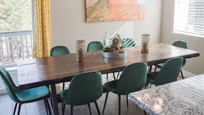 A dining area with a wooden table, green chairs, and a painting of a mountain.