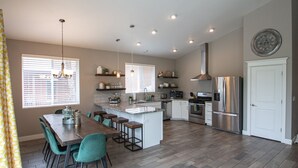 A modern kitchen with a central island, bar stools, and a dining table.