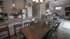 A modern kitchen with granite countertops, a wooden dining table, and green chairs.