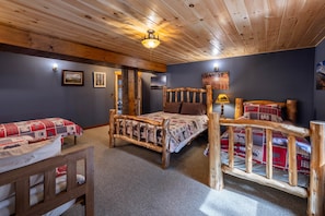 A cabin-style room with a wooden ceiling, a bed with a patterned bedspread, a wooden chair, and a small table. - River Road Loj - Lake Placid log cabin rental (Lake Placid)