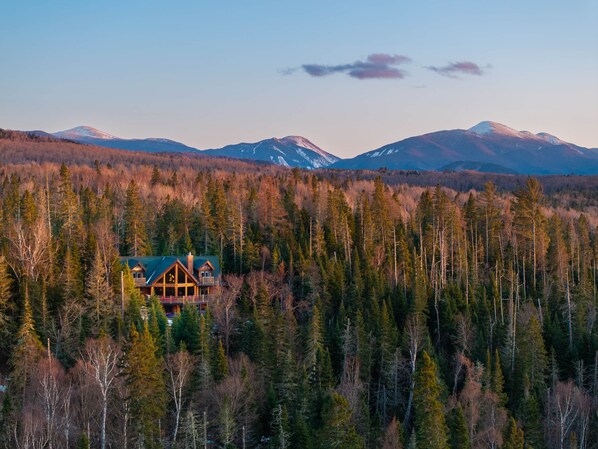 Un chalet entouré d’une forêt dense, avec des montagnes en arrière-plan.