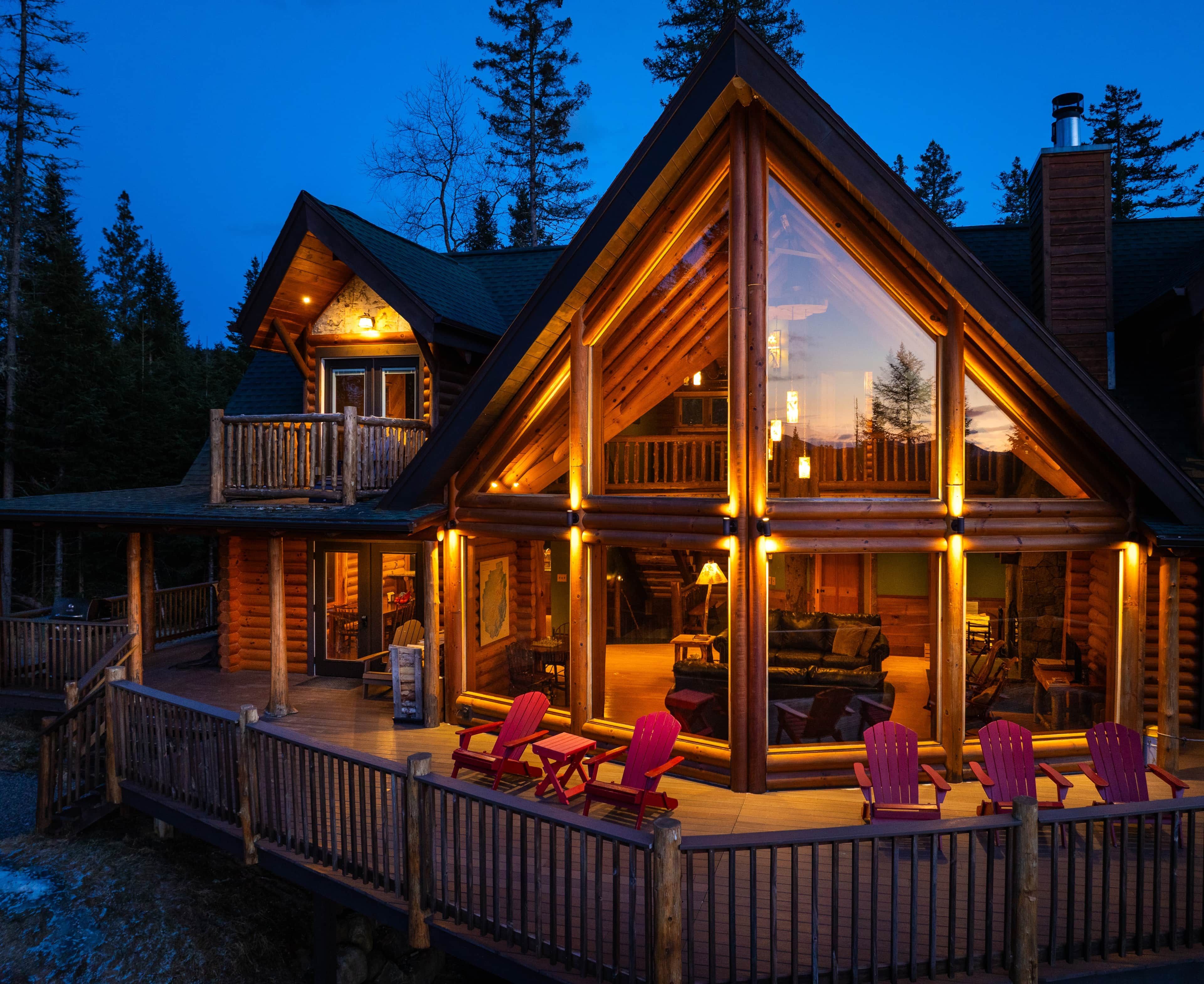 Une cabane en rondins dotée d’une grande terrasse, de nombreuses fenêtres et d’une cheminée.