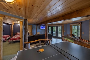 Una habitación con mesa de ping pong, sofá y mesa de futbolín. Hay dos camas con ropa de cama roja y blanca.