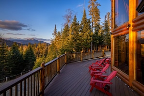 Una terraza de madera con sillas rojas que da a un paisaje montañoso cubierto de bosque.