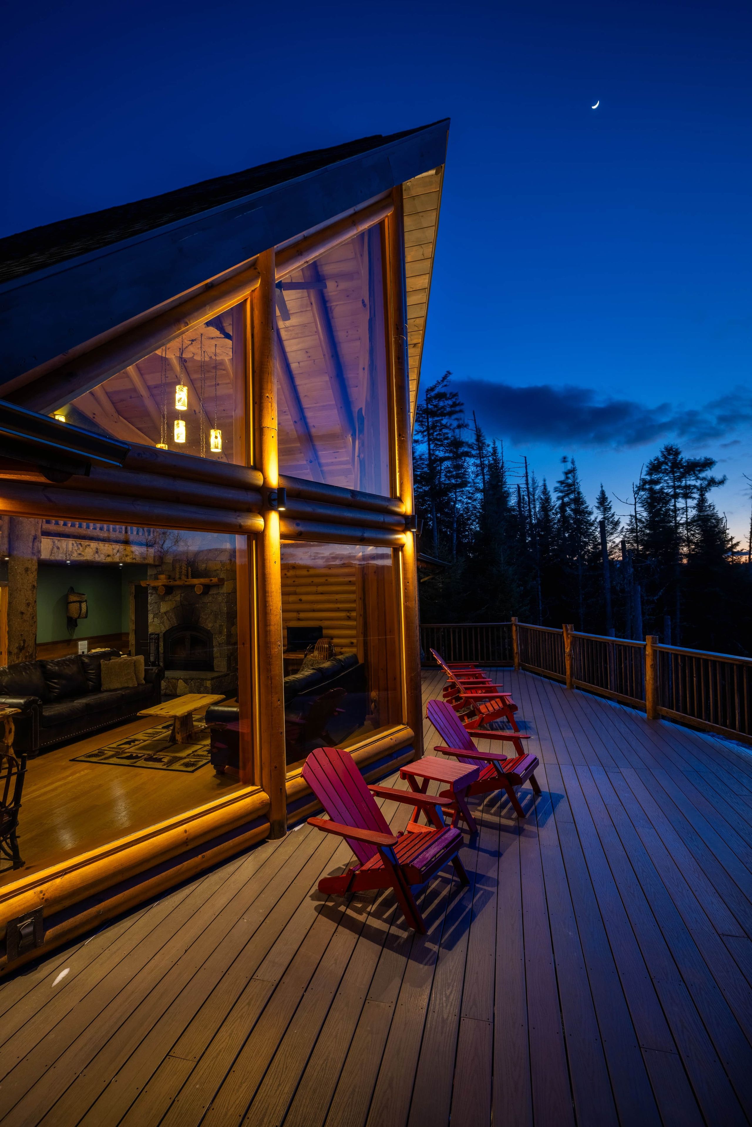 A wooden deck with red Adirondack chairs and a glass-enclosed room with a fireplace.