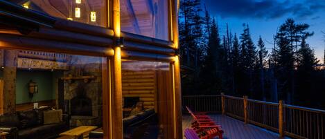 A wooden deck with red Adirondack chairs and a glass-enclosed room with a fireplace.