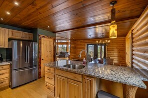 Une cuisine de style rustique, avec des meubles en bois, des appareils électroménagers en acier inoxydable, des plans de travail en granit et un luminaire suspendu.