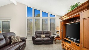 Un salón con un sofá de cuero marrón, un sillón reclinable y un mueble de entretenimiento de madera con televisor de pantalla plana.