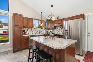 A modern kitchen with wooden cabinets, a large island, stainless steel appliances, and a view of the outside.