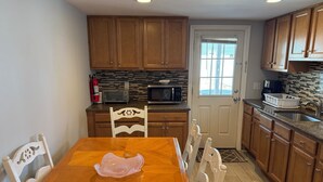 A kitchen with wooden cabinets, a granite countertop, a microwave, a toaster, and a dining table with chairs.