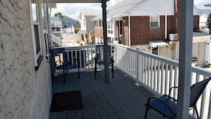 A covered porch with a white railing, two blue chairs, and a wooden bench.