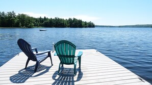 Un muelle de madera con dos sillas Adirondack mirando a un lago tranquilo, rodeado de un bosque frondoso.