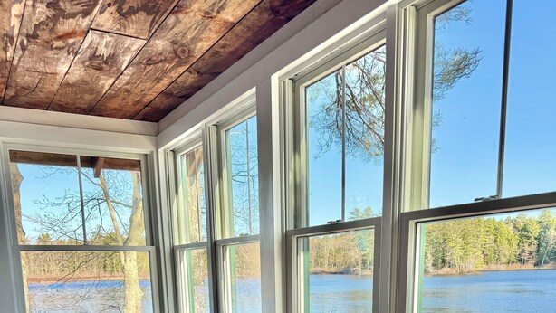 Una habitación con techo de madera, ventanas amplias, sillas de mimbre y vista a un lago.