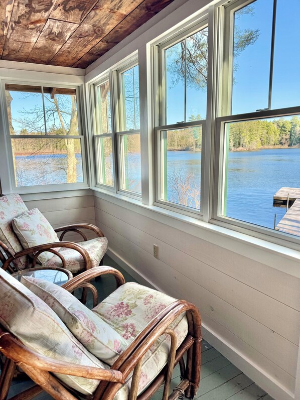 A room with a wooden ceiling, large windows, wicker chairs, and a view of a lake.