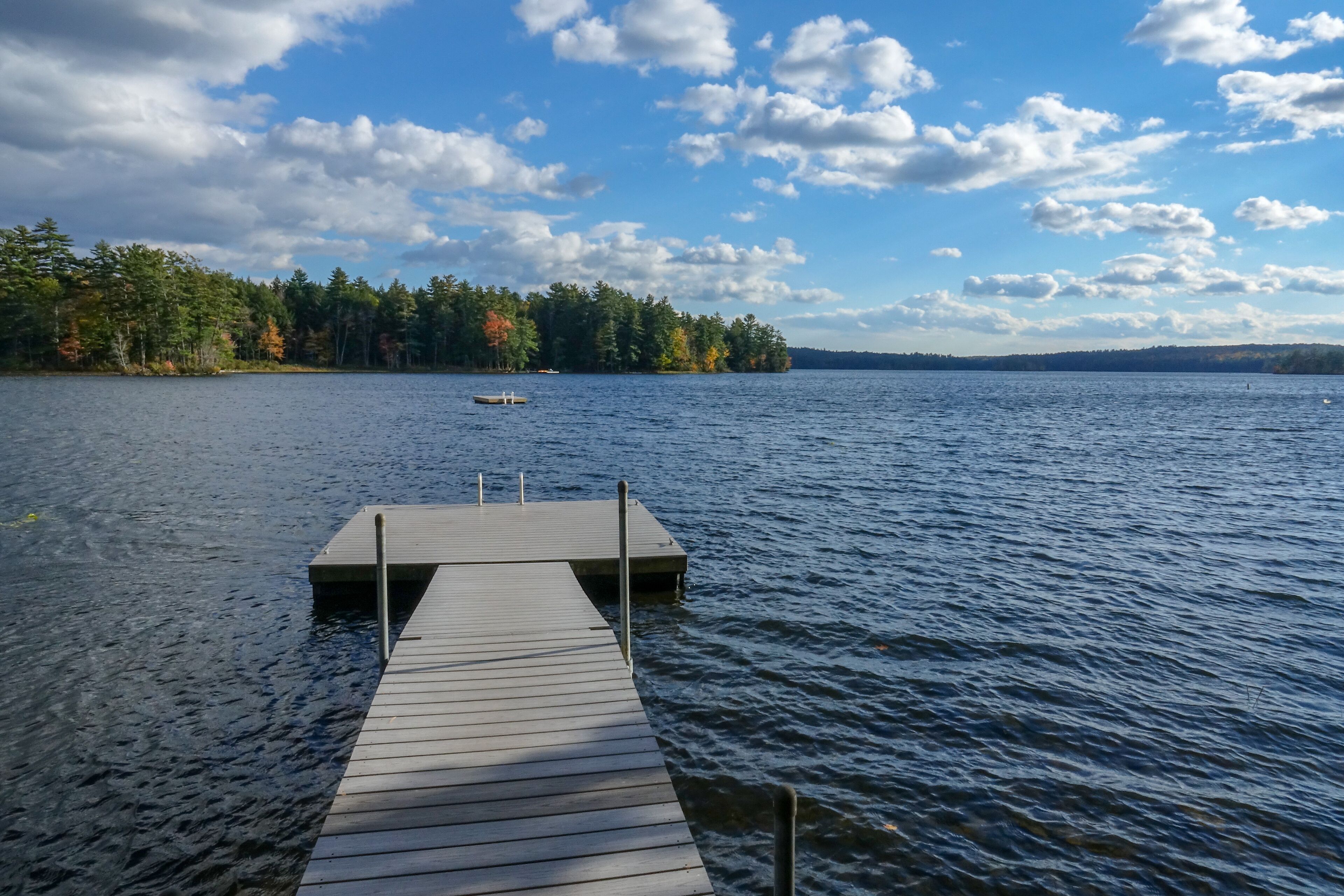 A wooden dock extending into a calm lake with a forested shoreline and a boat in the distance.