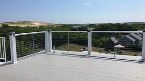 Una terraza de madera con barandas blancas que da a un área ajardinada con árboles y una vista distante de edificios.