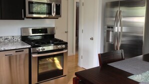 Una cocina moderna con electrodomésticos de acero inoxidable, una mesa de comedor de madera y una puerta blanca.