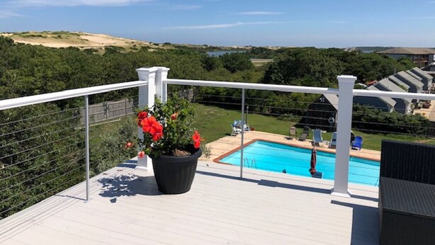 Una terraza con piscina, rodeada de follaje y un cielo despejado.