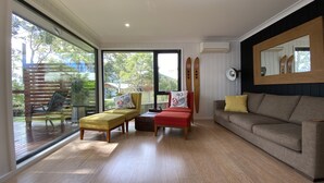 A spacious living room with a large sliding glass door leading to a deck, a sofa, two armchairs, and a small table. - Premium Waterfront - Jervis Bay Area (St Georges Basin)