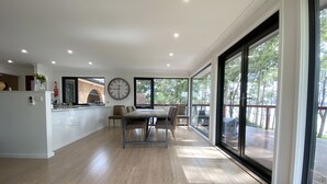 A spacious kitchen with a dining area, large windows, and a view of the outdoors. - Premium Waterfront - Jervis Bay Area (St Georges Basin)