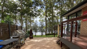 An outdoor patio with a grill, a table, and a view of the lake. - Premium Waterfront - Jervis Bay Area (St Georges Basin)