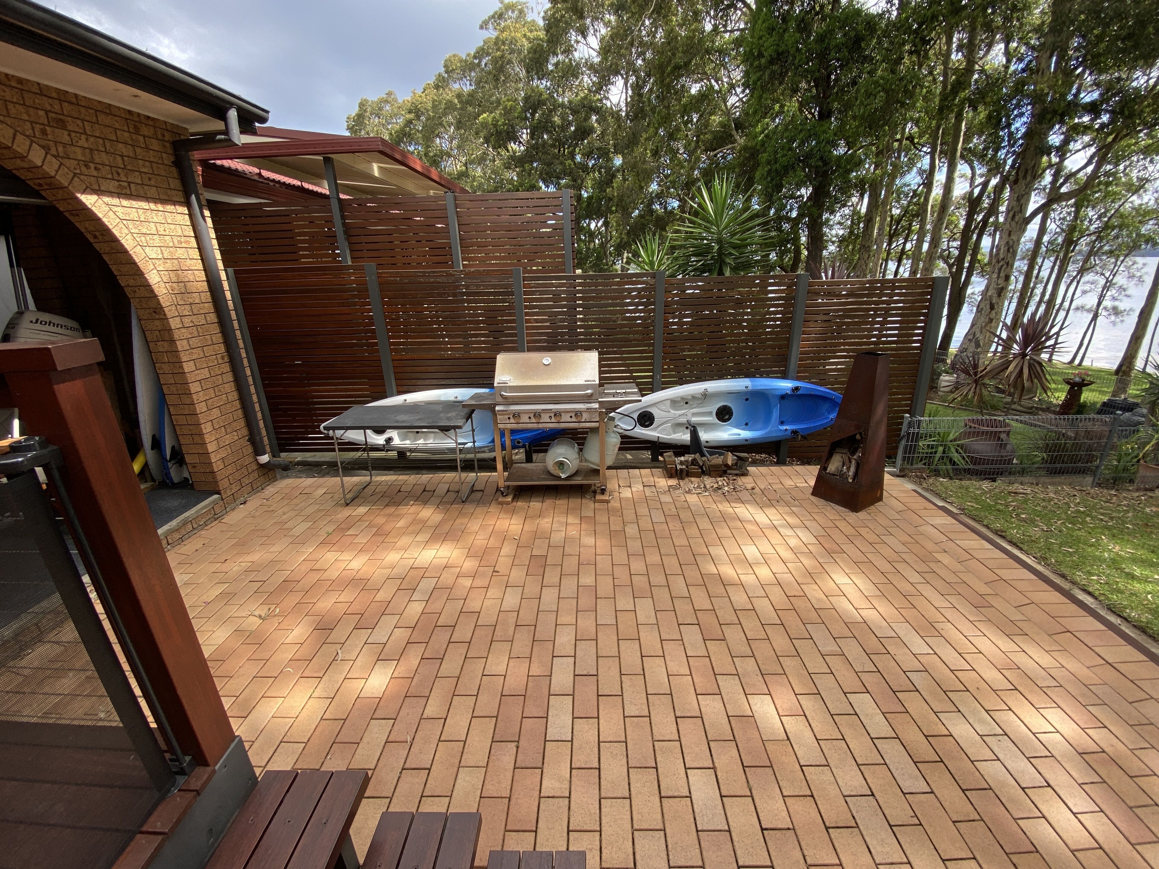 A patio with a barbecue grill, two kayaks, and a wooden fence.