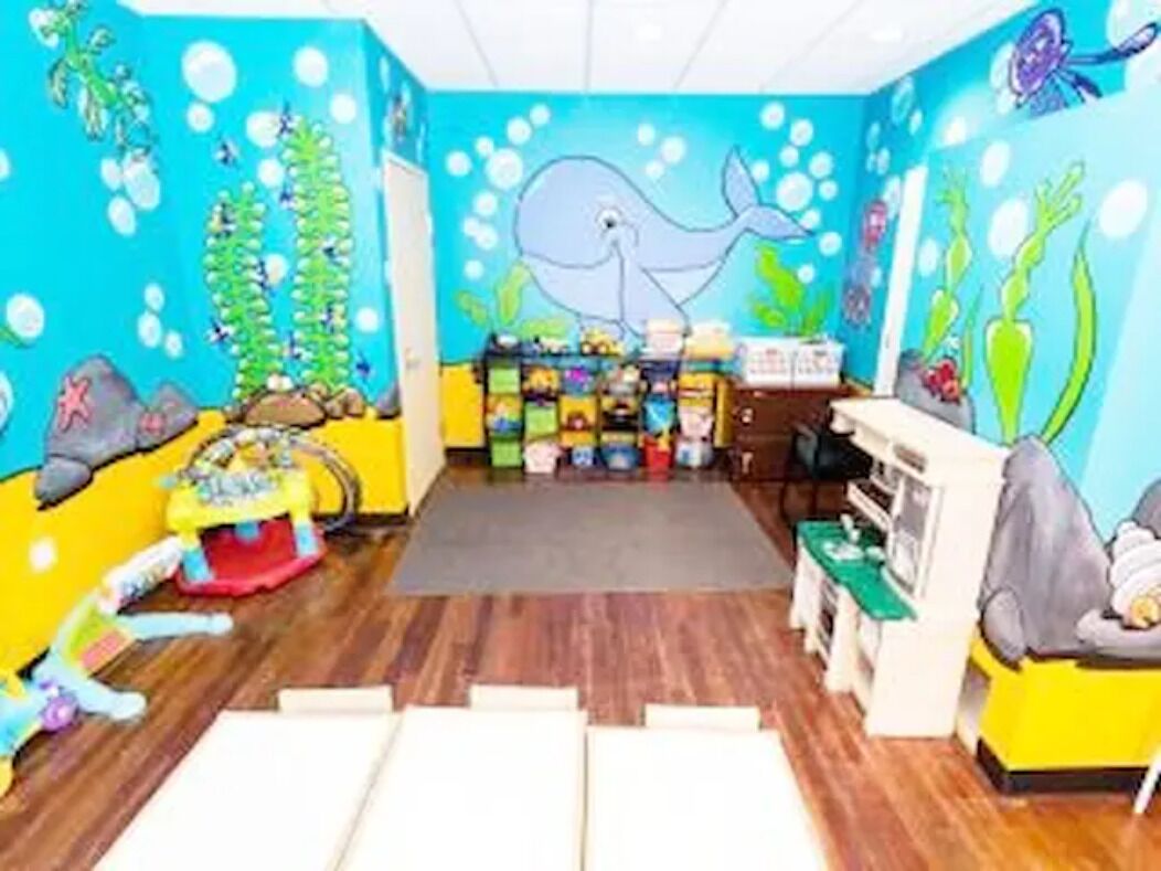 A room with a blue ocean-themed mural, wooden flooring, a play area with toys, and a small table with chairs.