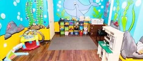A room with a blue ocean-themed mural, wooden flooring, a play area with toys, and a small table with chairs.