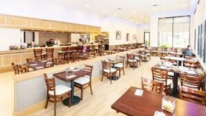 Ein geräumiges Restaurant mit mehreren Tischen und Stühlen, einer Theke mit Barbereich und großen Fenstern, die viel Tageslicht hereinlassen.