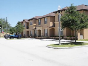 A residential building with multiple balconies, a clear sky, and a blue vehicle parked on the street. - 3 mile to Disney, 1 min Walk to Pool/Slides, Free WiFi, Behind OldTown &Fun Spot (Kissimmee)
