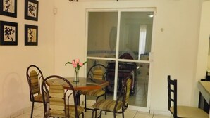 Un coin repas avec une porte vitrée donnant sur un balcon, une table avec des chaises et des tableaux encadrés accrochés au mur.