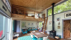 Un vaste espace de vie aménagé dans un style industriel, avec un plafond haut, un escalier en bois, une table à manger et une cheminée.