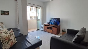 Ein Wohnzimmer mit zwei schwarzen Sofas, einem Fernseher auf einem Holzboden und einer Glastür, die auf einen Balkon führt.