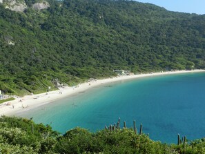 A coastal beach with a sandy shore, clear turquoise waters, and lush green hills in the background. - Apartment in Prainha, 4 minutes from the beach (Arraial do Cabo)