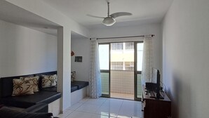 Ein Wohnzimmer mit einer Couch, einem Deckenventilator und Blick durch eine Schiebetür auf einen Balkon.