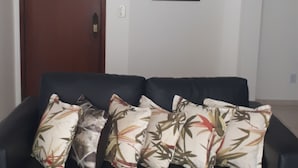 Ein Wohnzimmer mit einem dunkelgrauen Sofa, mehreren gemusterten Kissen, einem Deckenventilator, einer Holztür und einer gerahmten Karte an der Wand.