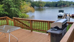 Een terras met een barbecue en een stoel, met uitzicht op een meer met boten en huizen op de achtergrond.