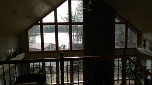 Een kamer met een groot erkerraam dat uitkijkt op een besneeuwd landschap, een houten trap en een plafondventilator.