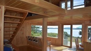 Uma cabana de madeira com escadas, um banco e área de refeições com vista para o lago.
