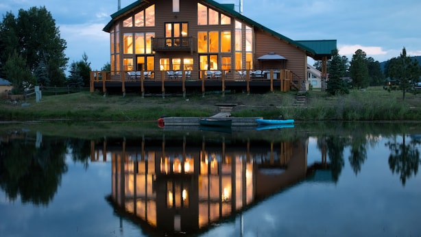 A large wooden cabin with a balcony, situated by a calm lake.